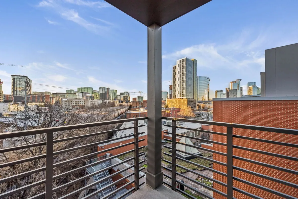 An elevated perspective overlooking Nashville’s contemporary skyline, as seen from behind a balcony or terrace railing. The city’s architecture and street life are in clear view, evoking the energy and accessibility of the neighborhood.