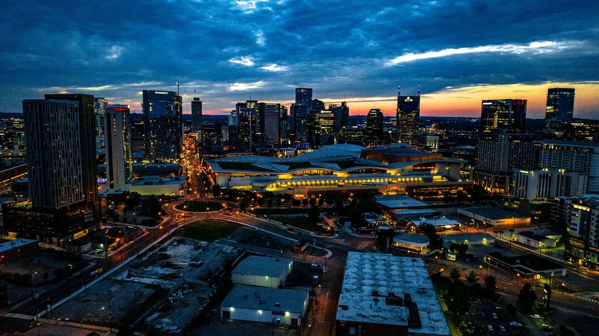 A wide city skyline view at sunset, with glowing street lights and the convention center in the background. The scene is energetic and inviting, representing the urban excitement just beyond the building.