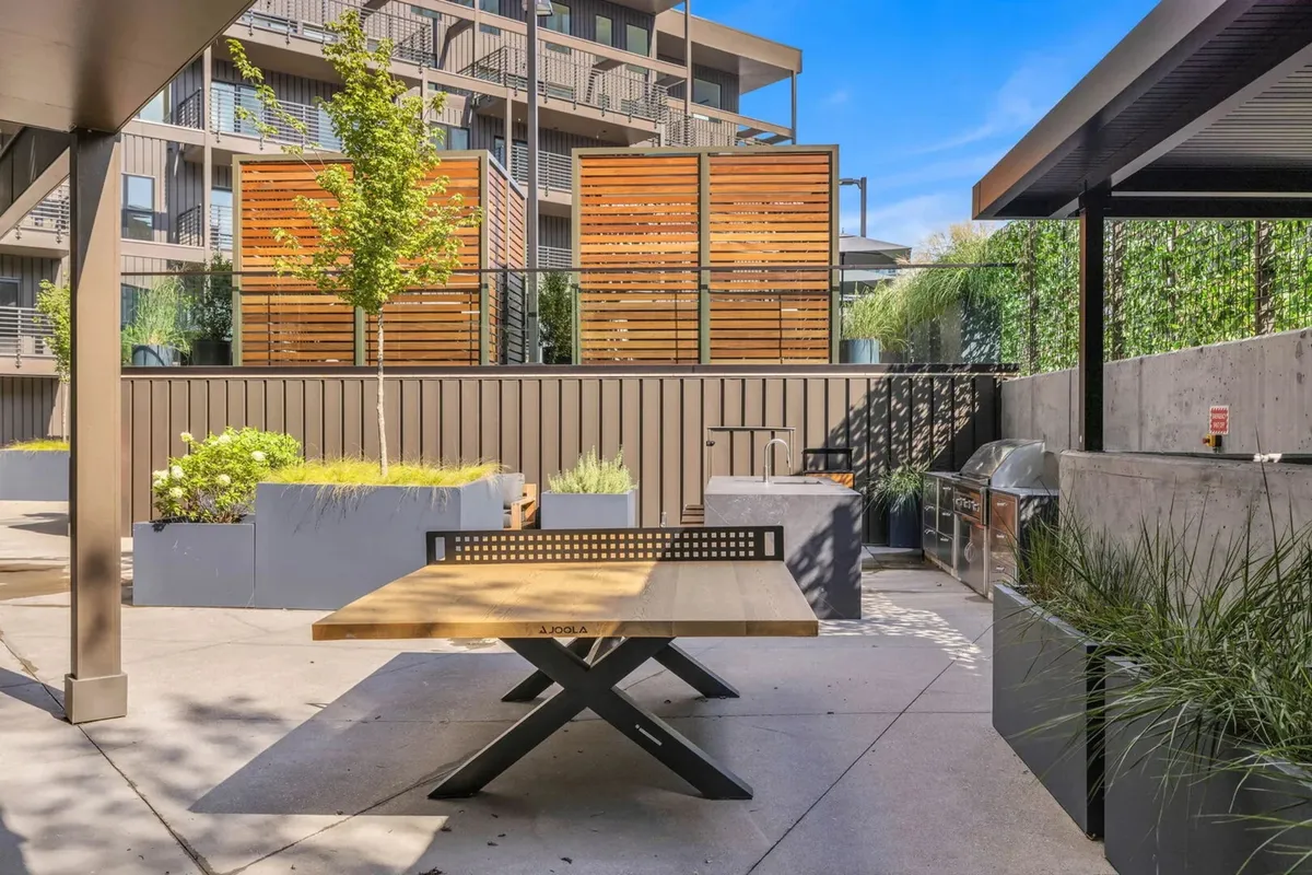 A cozy outdoor picnic area featuring a wooden table, surrounding planters filled with lush greenery, and privacy screens. The space is inviting for outdoor dining, barbecues, or relaxed gatherings with friends and family.