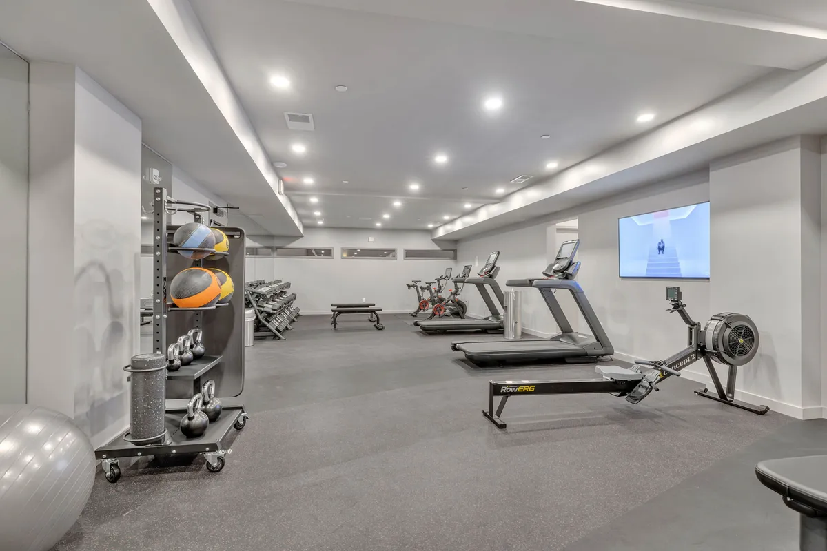 A state-of-the-art fitness center equipped with treadmills, stationary bikes, rowing machine, dumbbells, exercise balls, and a clean, bright interior. The space invites for both solo workouts and group fitness sessions.