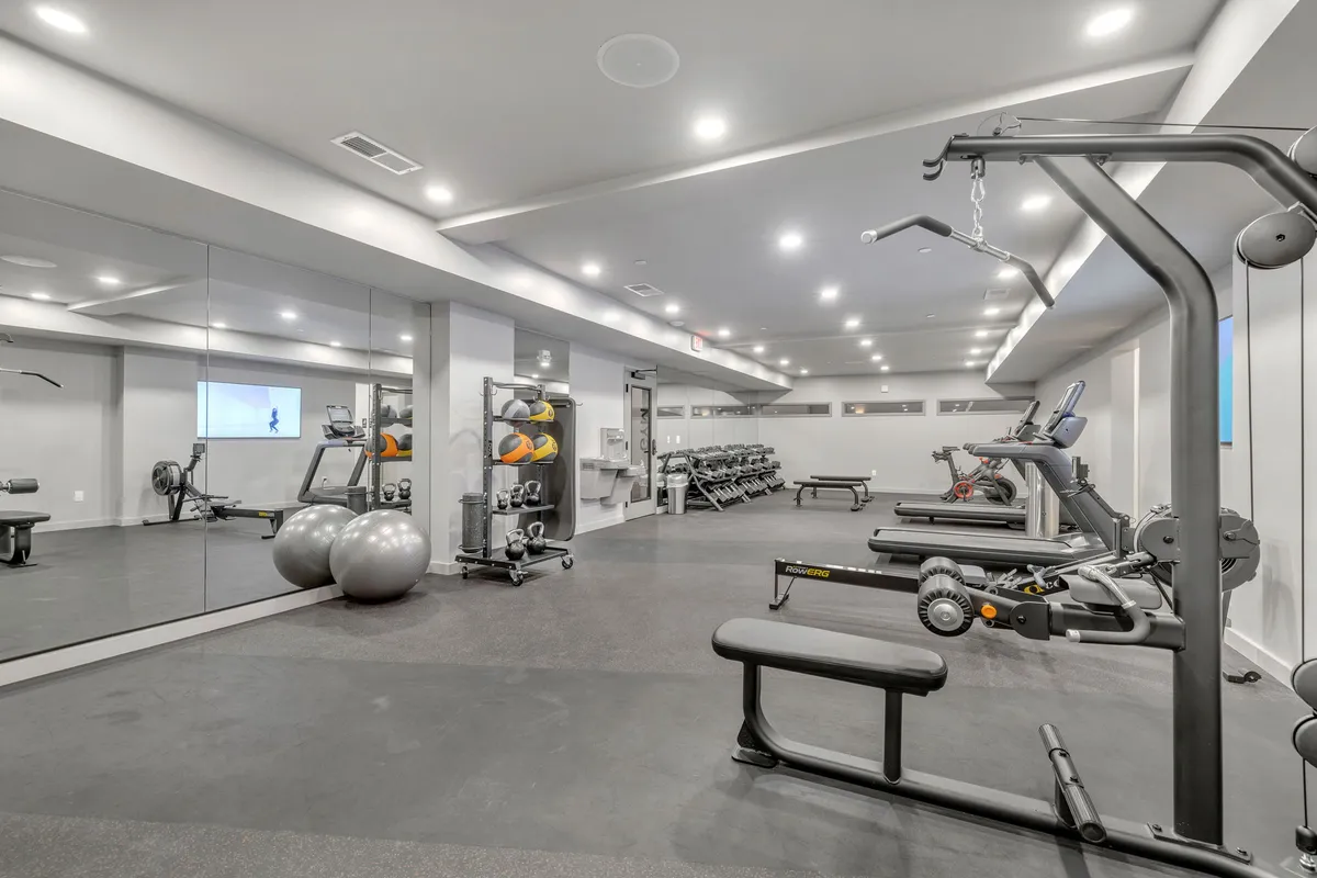 A modern, well-equipped fitness center filled with exercise machines, free weights, and large mirrors. The clean, motivational space suggests an active, health-conscious lifestyle within easy reach.