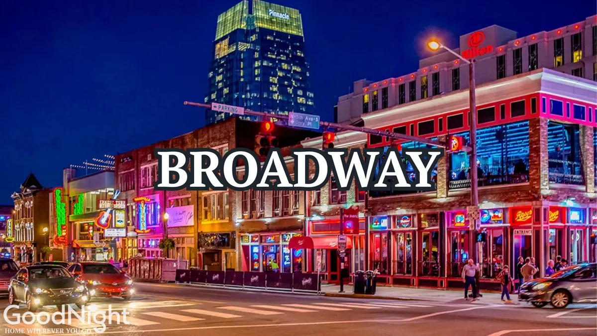 This exterior shot captures Nashville’s lively urban streets at night, dotted with neon signs, bustling pedestrians, cars, and high-rise buildings. The energy and vibrancy of the Broadway area are apparent, showcasing one of the city's entertainment hotspots.