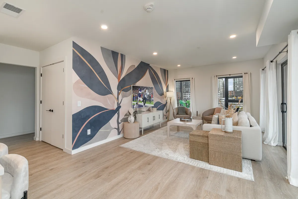 A comfortable living area featuring a large wall mural, a flat-screen television, stylish seating, and decorative accents on the table. The space radiates a relaxed, contemporary vibe ideal for game nights, movie marathons, or creative conversations.