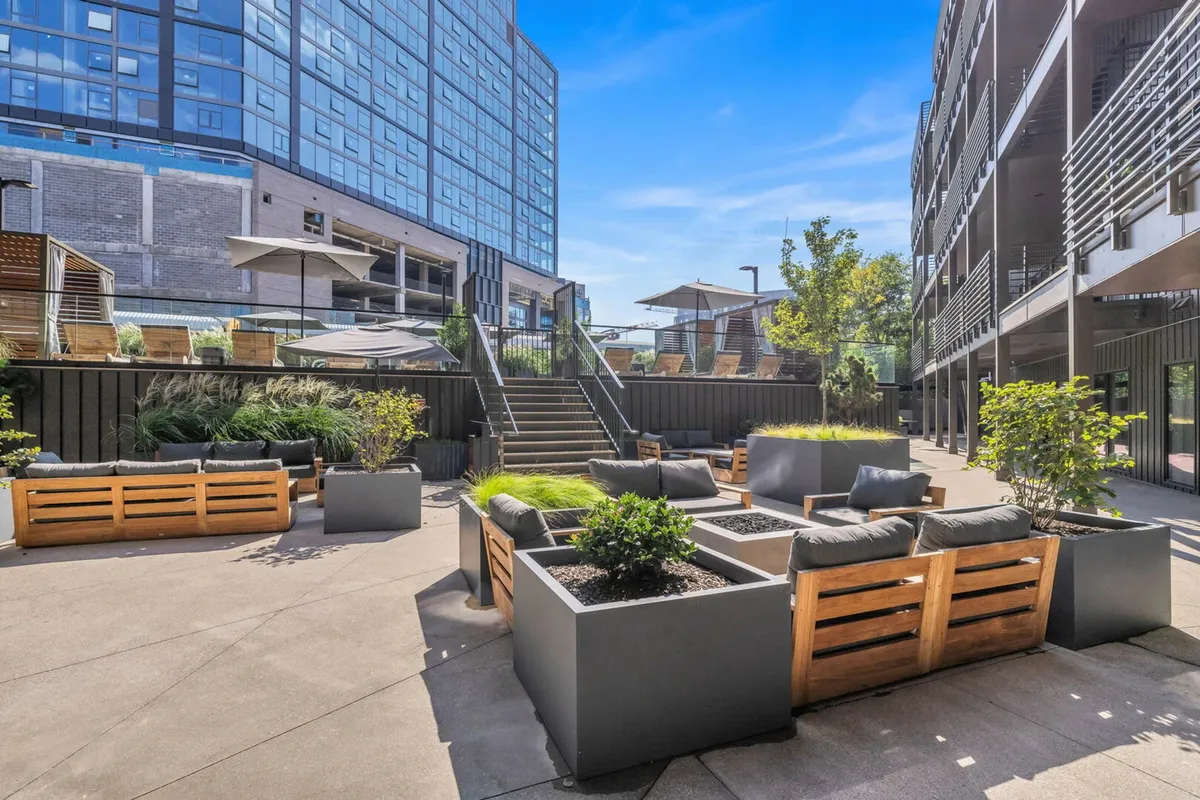 Contemporary outdoor seating areas surrounded by planters with greenery and a staircase leading to upper levels. The space feels open and communal, ideal for relaxing or socializing outdoors.